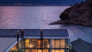 Un bâtiment moderne à la façade vitrée, donnant sur une étendue d’eau, et entouré de verdure et d’édifices à l’architecture traditionnelle.