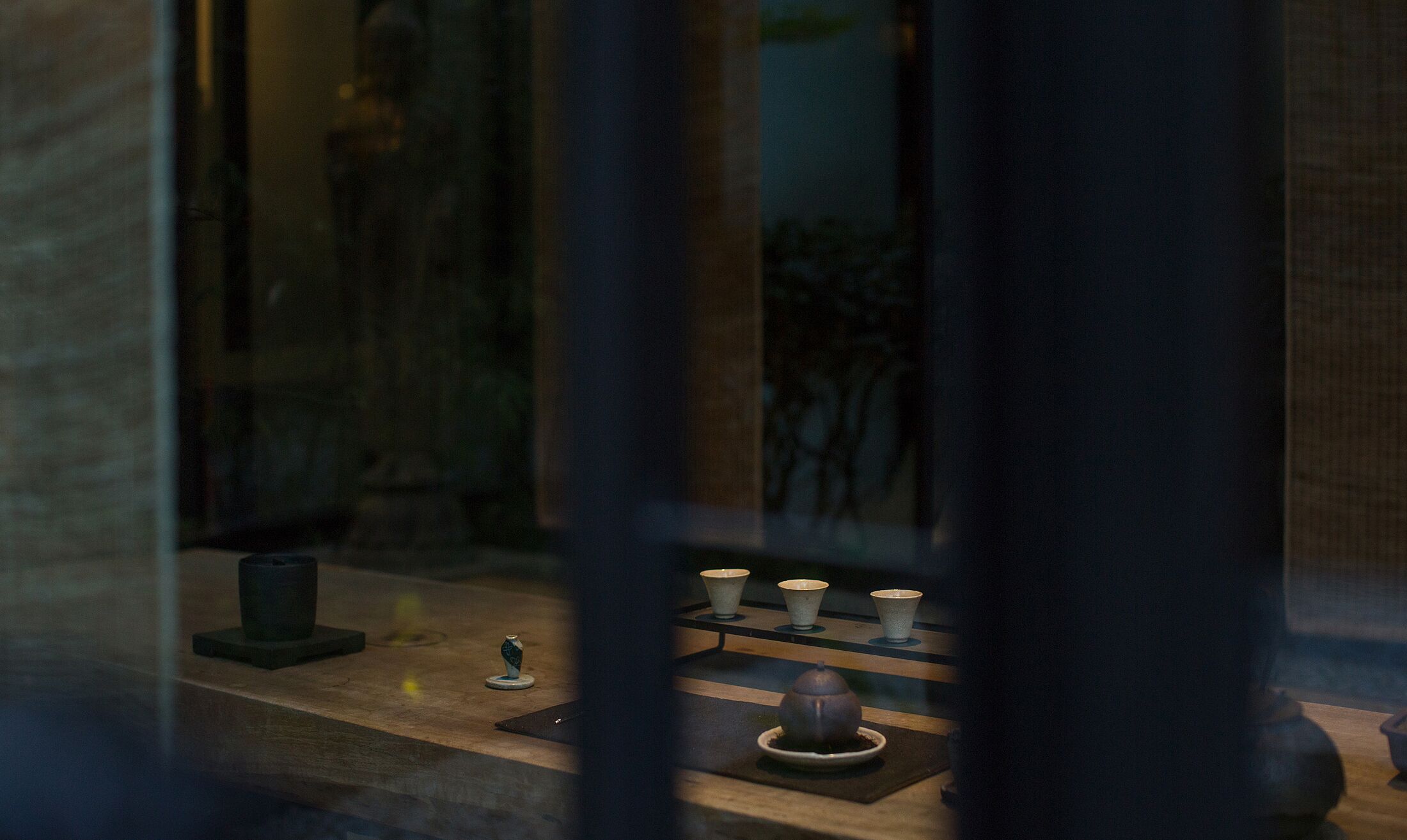A dimly lit room with a wooden table displaying a tea set, including cups and a teapot.