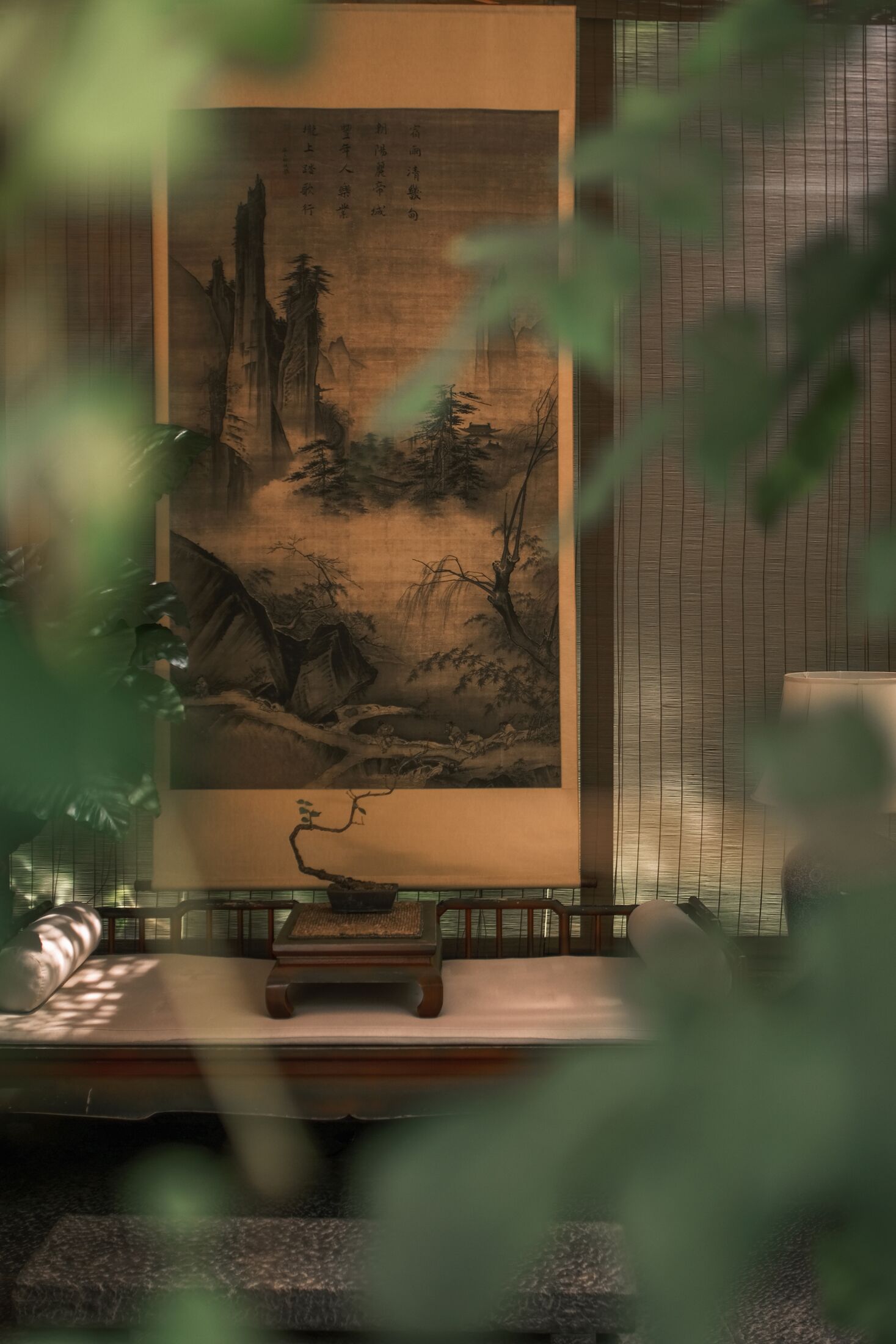 A traditional room with a large calligraphy scroll, a wooden bench, and a bamboo screen.