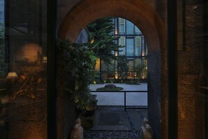 An arched entrance leading to a courtyard with a modern building in the background, surrounded by potted plants and a stone pathway.
