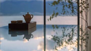 Una mesa con un juego de té y tazas, reflejando una vista de montañas y árboles a través de una ventana.
