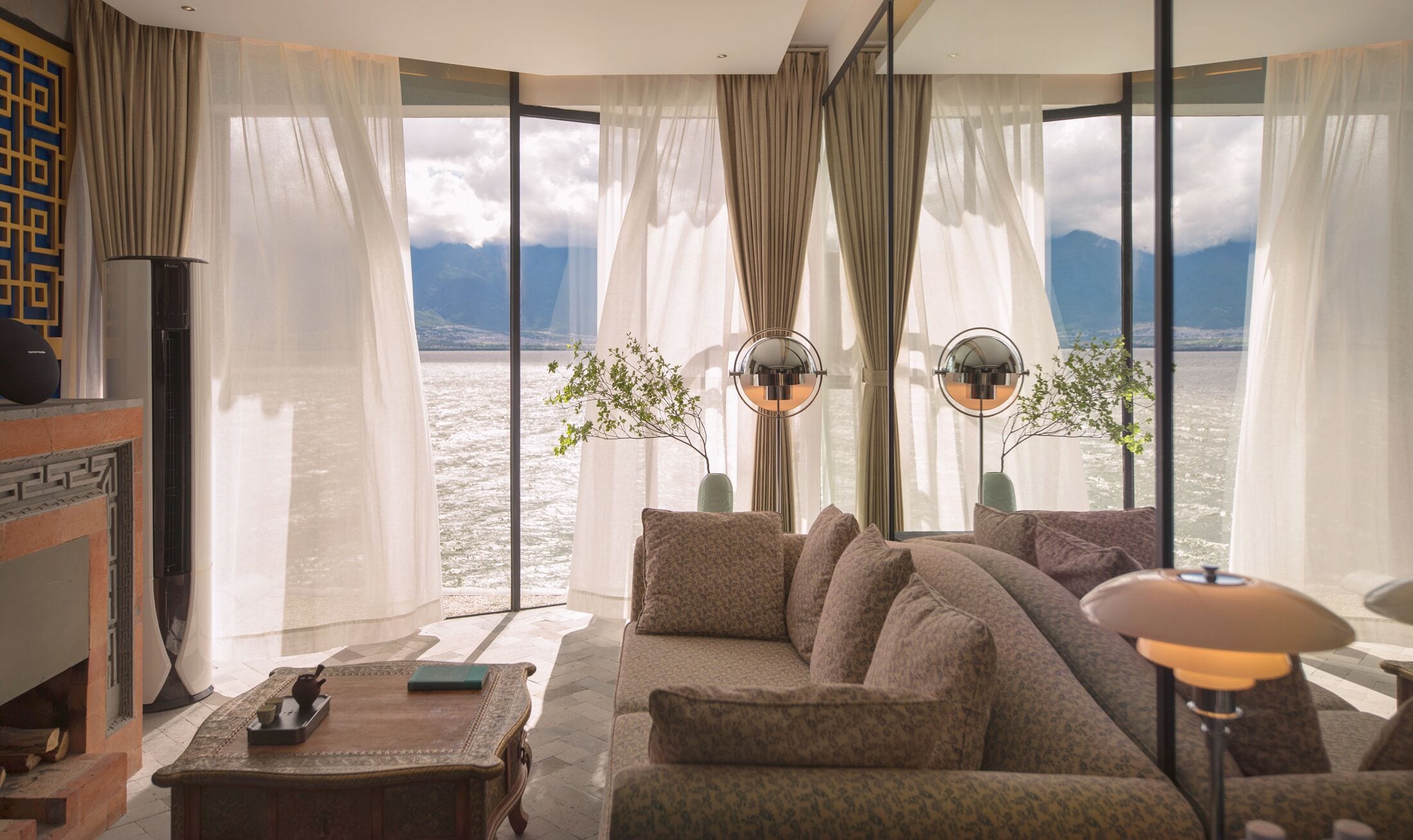 Una sala de estar moderna con un sofá grande, una mesa de centro y vista a un lago con montañas al fondo.