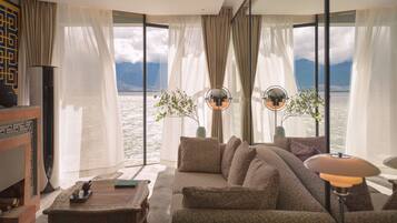 Una sala de estar moderna con un sofá grande, una mesa de centro y vista a un lago con montañas al fondo.