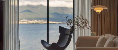 Un salón moderno con vistas al mar y a las montañas, una silla negra, un sofá beige y una lámpara de pie.