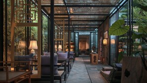 Un espace intérieur aménagé avec des coins salon, des tables et une paroi vitrée donnant sur la verdure à l’extérieur.