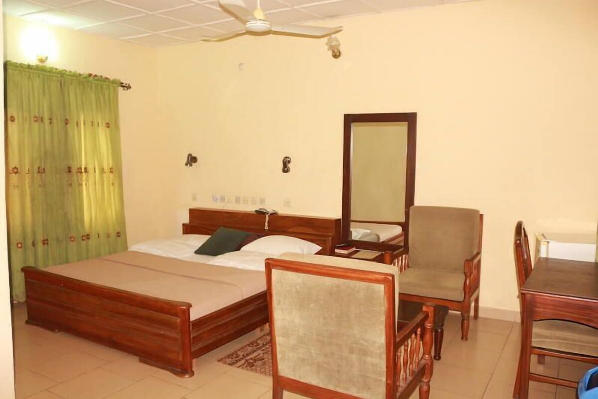 Une chambre à coucher comprenant un lit, une chaise, une table, un ventilateur de plafond et un miroir.