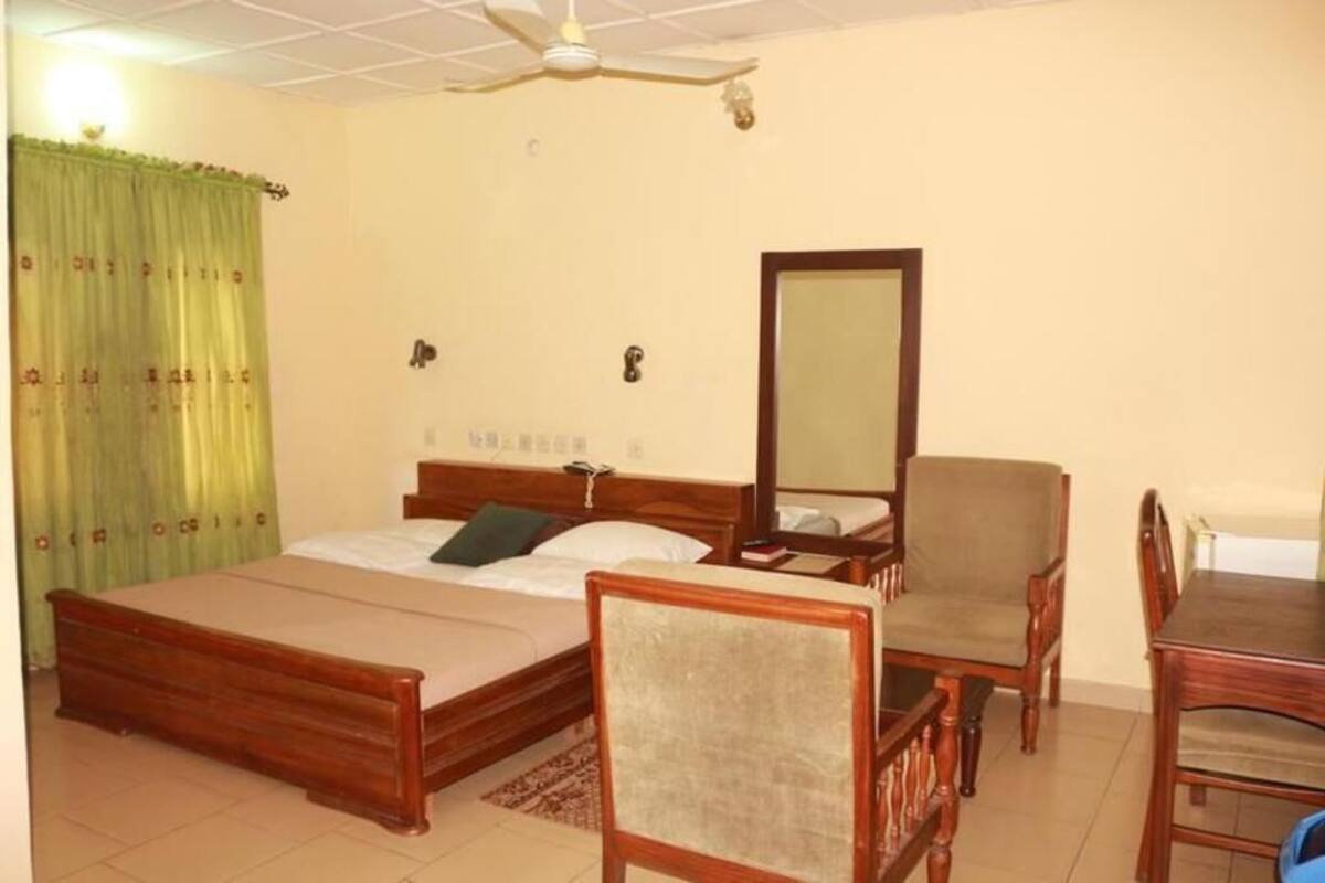 Une chambre à coucher comprenant un lit, une chaise, une table, un ventilateur de plafond et un miroir.