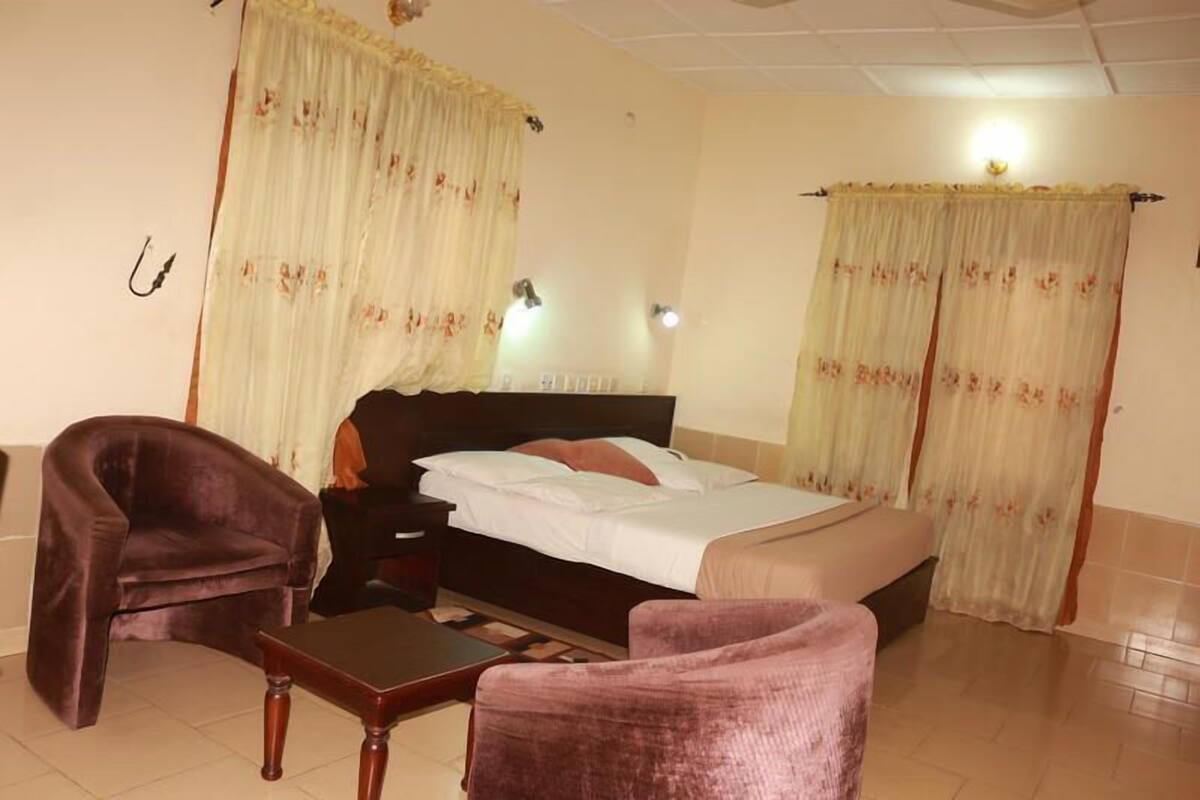 Une chambre d’hôtel avec un lit, deux chaises, une table de chevet et des rideaux.