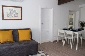 Un salon moderne avec un canapé gris, des coussins jaunes, une table à manger avec des chaises blanches et un tableau encadré au mur.