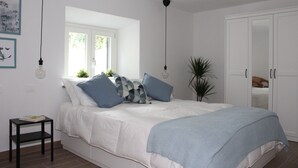 A bedroom with a bed, a window, a wardrobe, and a small table.