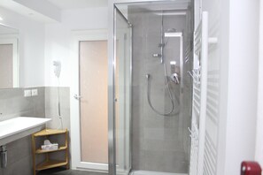 Une salle de bain moderne avec une douche à parois de verre, un lavabo blanc et une étagère en bois.