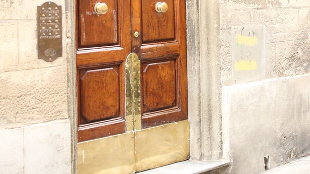 A wooden double door with a brass doorknob and a decorative metal arch above it.