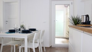 A dining area with a white table and chairs, a coffee maker on the counter, and a door leading to another room.