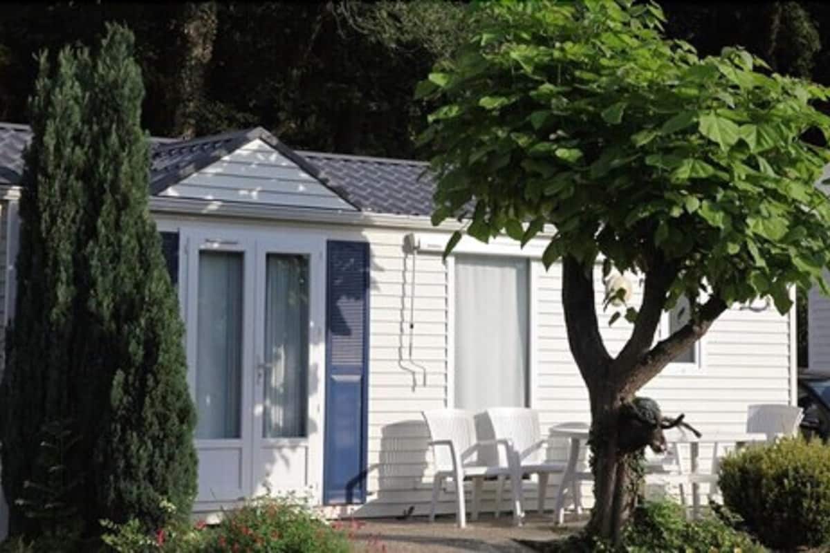 Una casa de un piso con un porche cubierto, un árbol grande y un jardín pequeño.