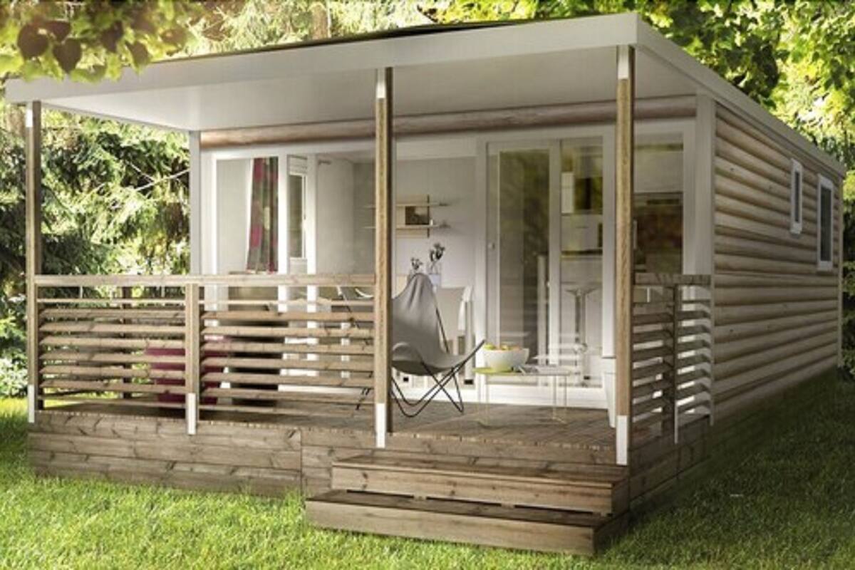 A modern, single-story cabin with a covered porch, a small seating area, and a visible bathroom.