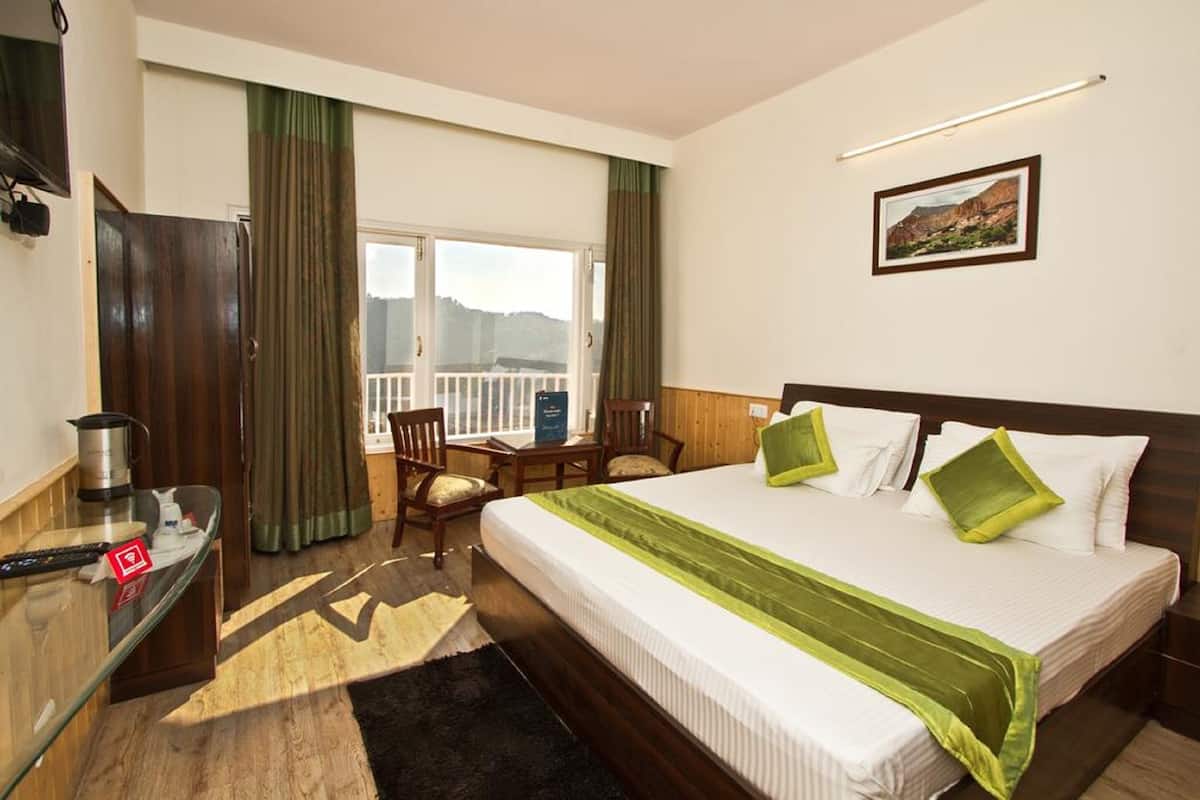 A hotel room with a bed, a desk, a chair, a window with curtains, and a painting on the wall.