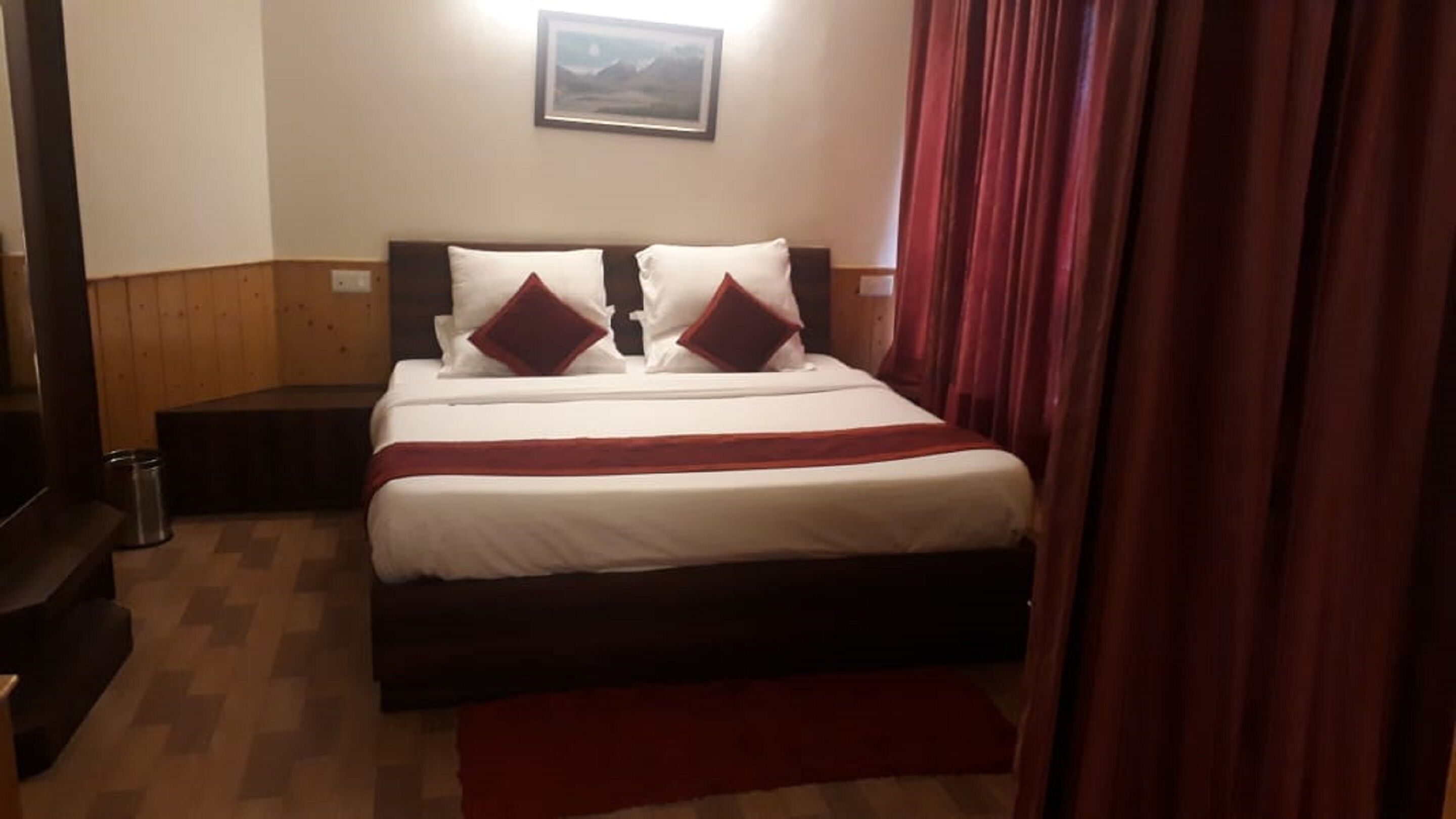 A neatly made bed with white and red bedding, a wooden headboard, and a small bedside table with a lamp.