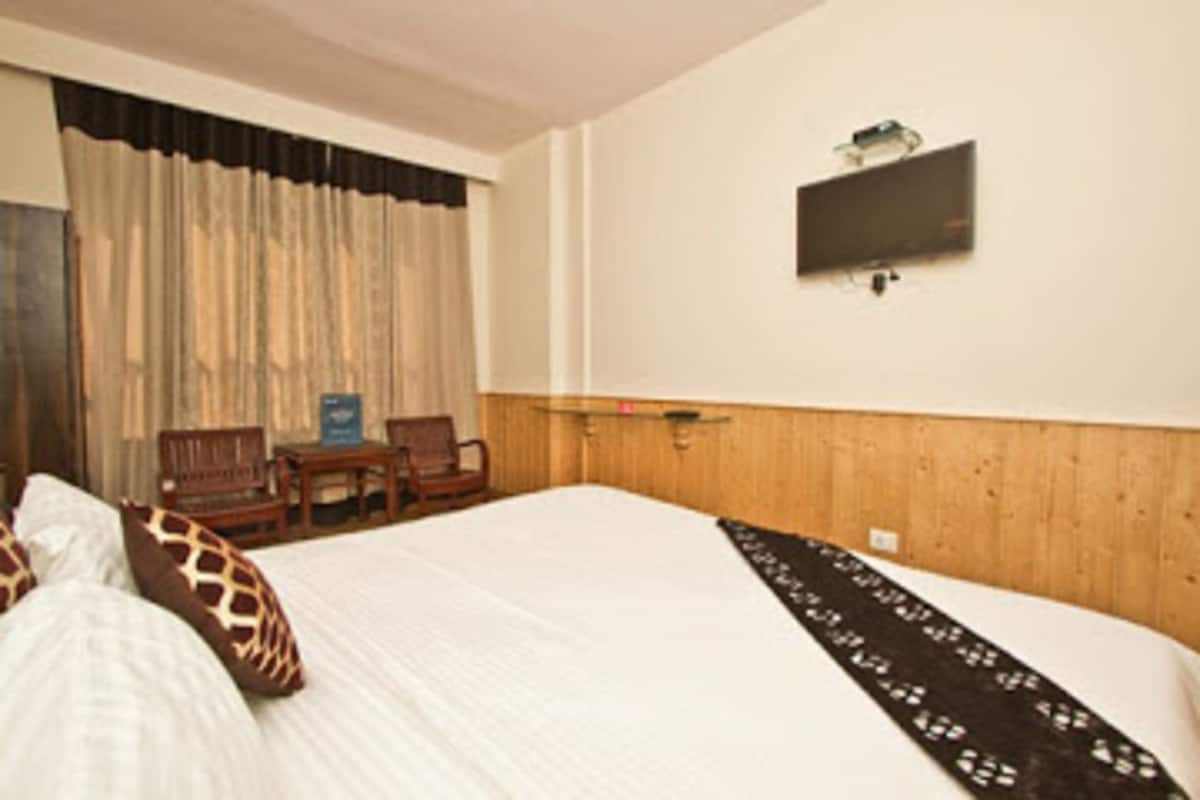 A hotel room with a bed, a television mounted on the wall, and a wooden headboard.