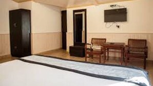 Una habitación con una cama, un escritorio, dos sillas y un televisor en la pared.