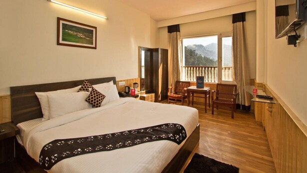 Habitación de hotel con una cama grande, un escritorio, una silla y un balcón con vistas a las montañas.
