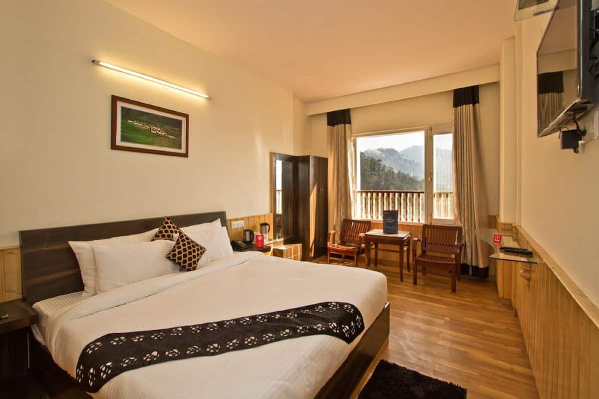 A hotel room with a large bed, a desk, a chair, and a balcony with a view of the mountains.