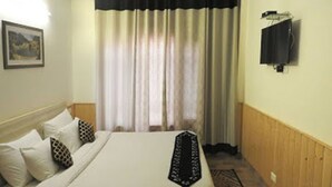 Una habitación de hotel con cama, almohadas, una alfombra, un televisor montado en la pared y un cuadro.