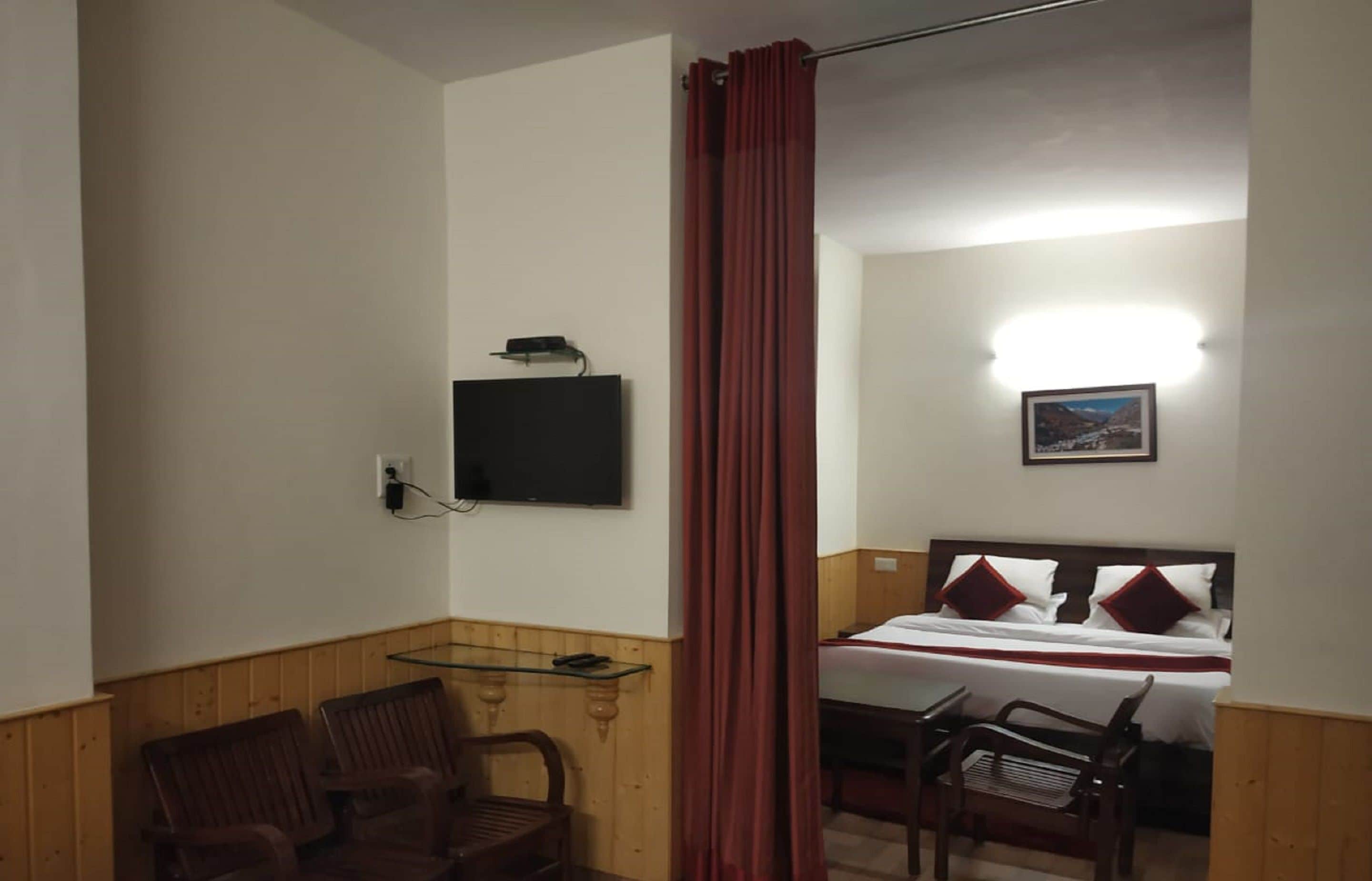 A room with a bed, a TV mounted on the wall, a small table, and two chairs.