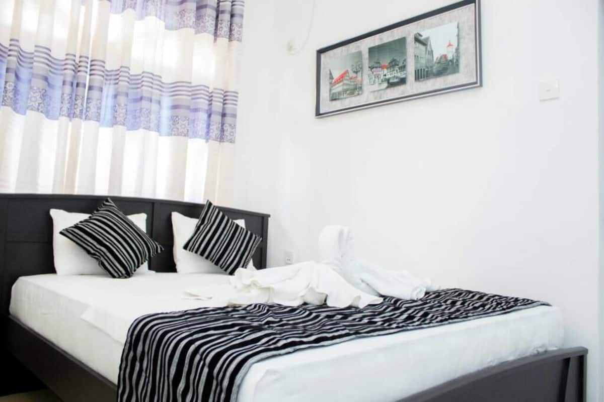 Uma cama bem arrumada com roupa de cama listrada, cabeceira e um quadro emoldurado na parede.