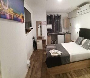 Een compacte hotelkamer met een bed, een klein bureau, een spiegel en een kitchenette.