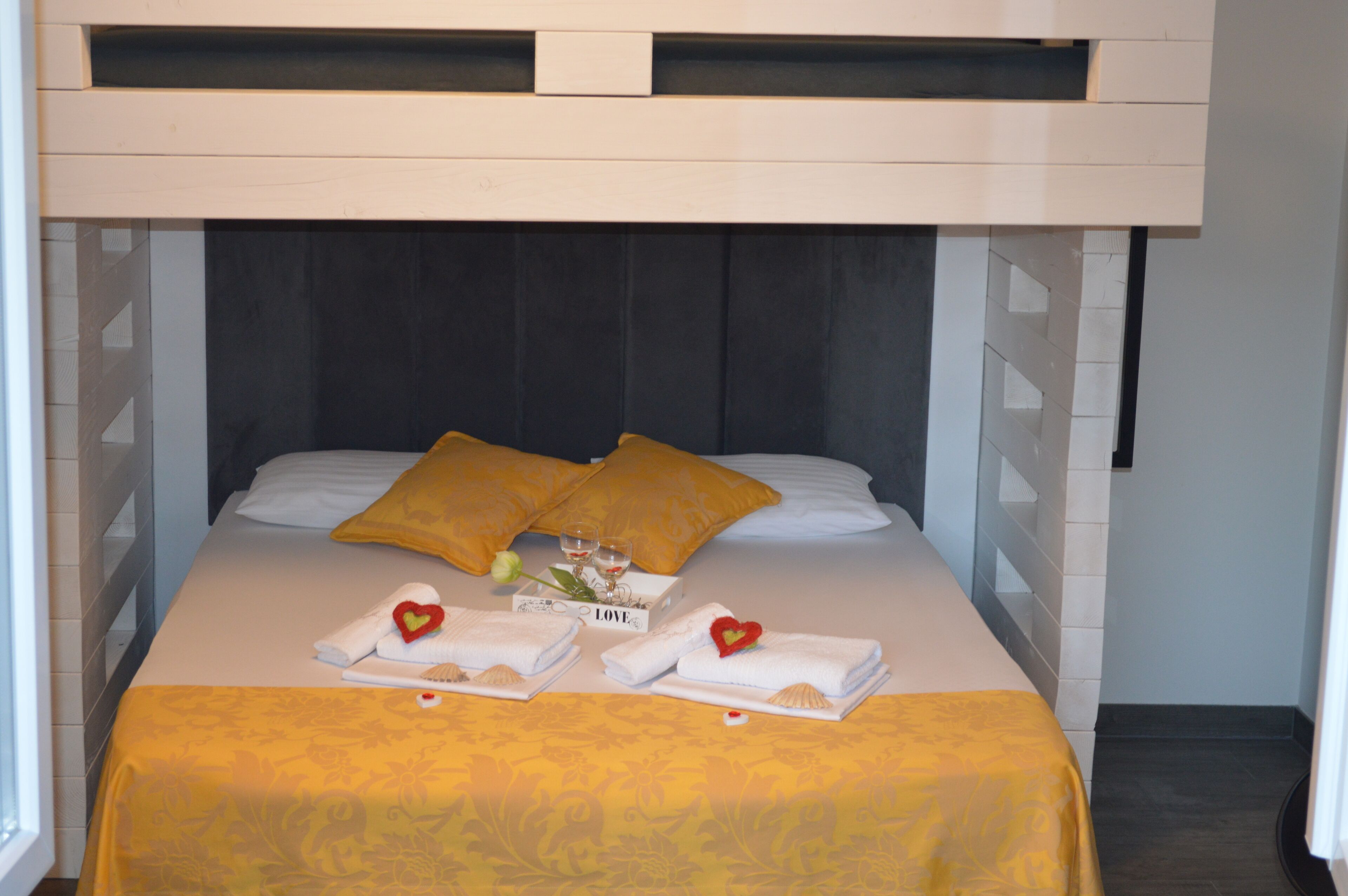 A neatly made bed with a yellow bedspread, two pillows, and a bouquet of flowers.