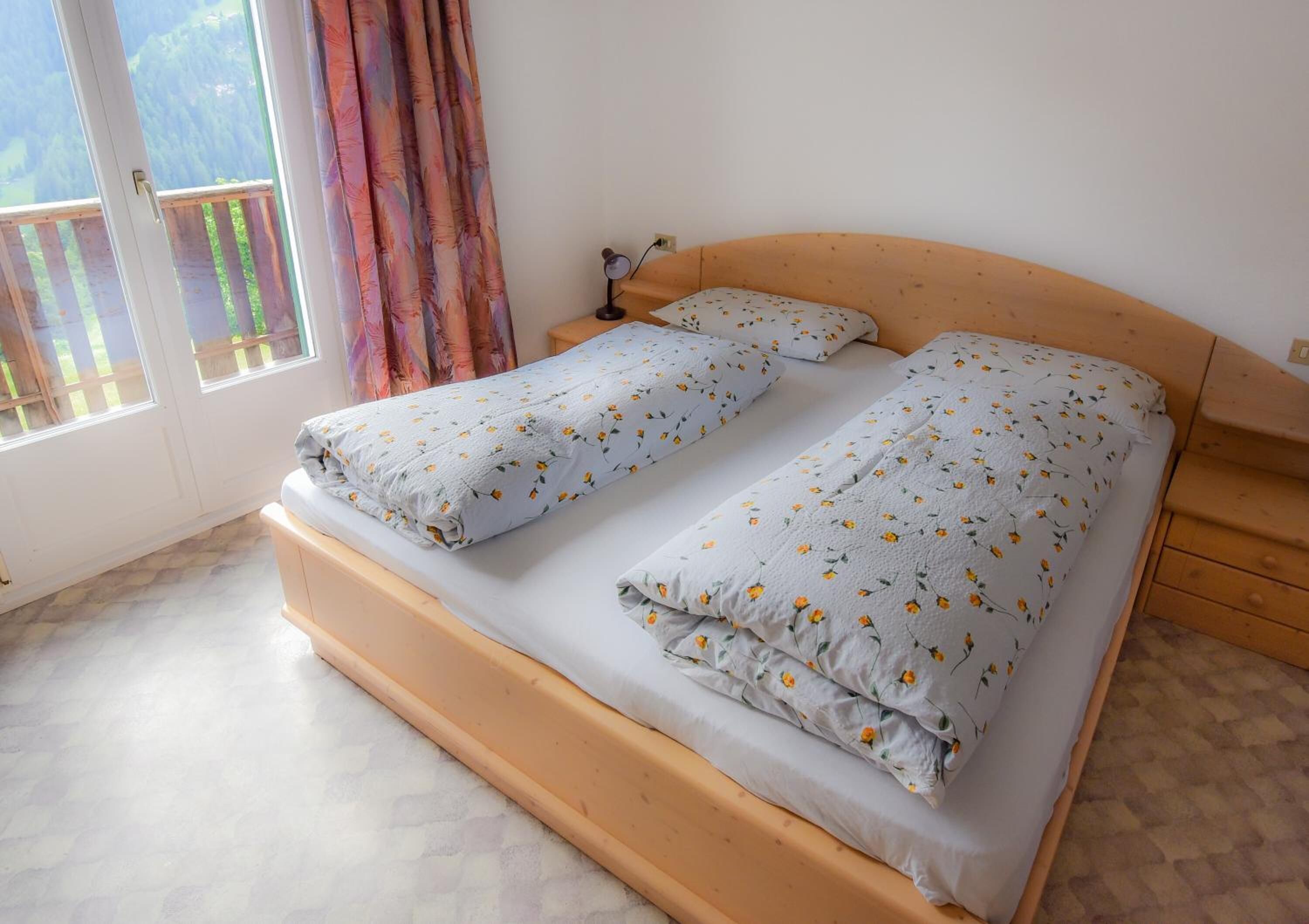 Ein Doppelbett mit floralem Bettbezug, ein Holz-Kopfteil und ein Nachttisch mit Lampe.