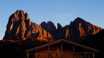 Eine rustikale Holzhütte mit schlichtem Satteldach, eingebettet in eine gebirgige Landschaft mit felsigem Untergrund.