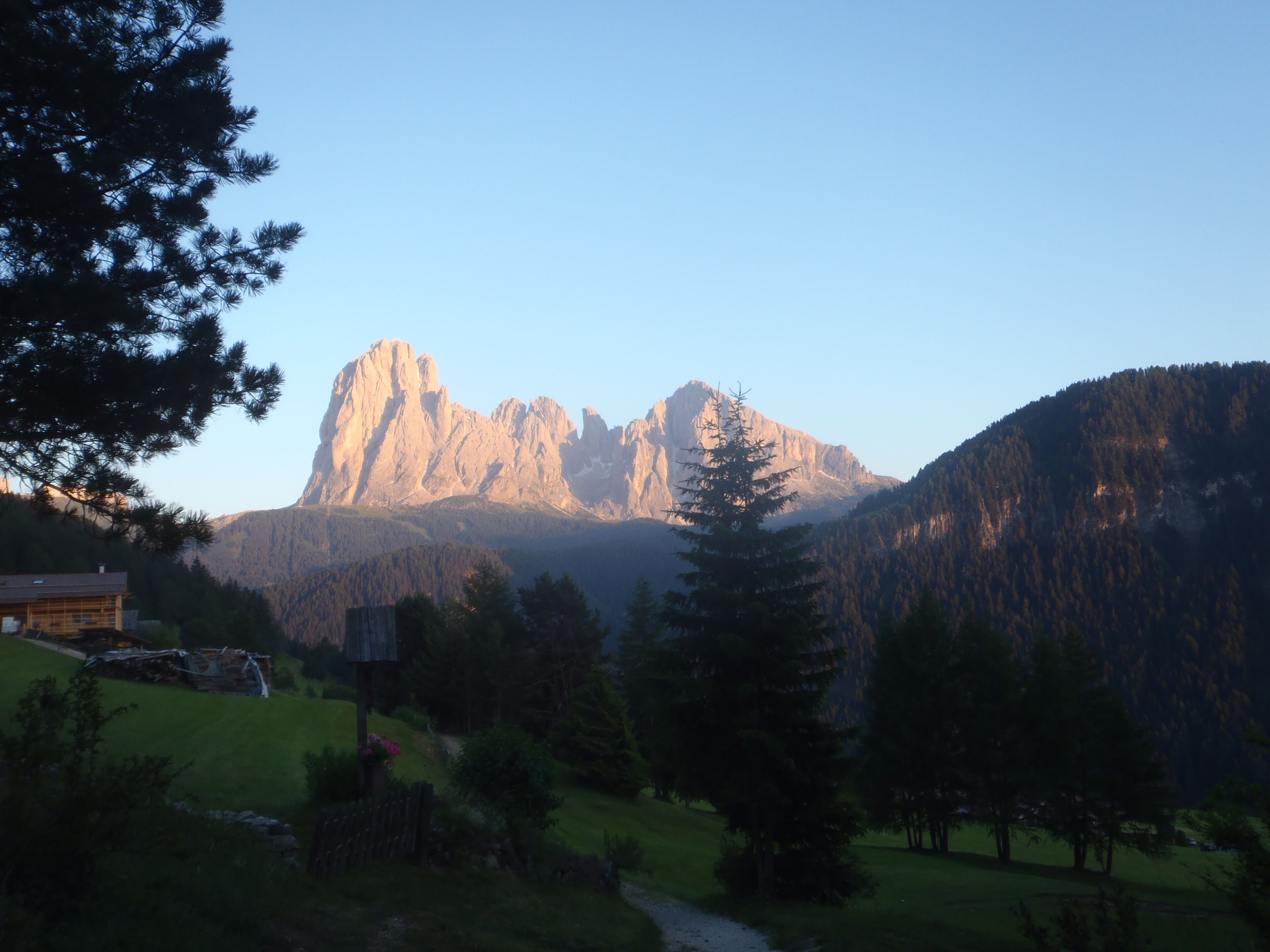 Eine Berglandschaft mit einem markanten Gipfel, einer Holzhütte und einem Pfad, der durch einen bewaldeten Bereich führt.