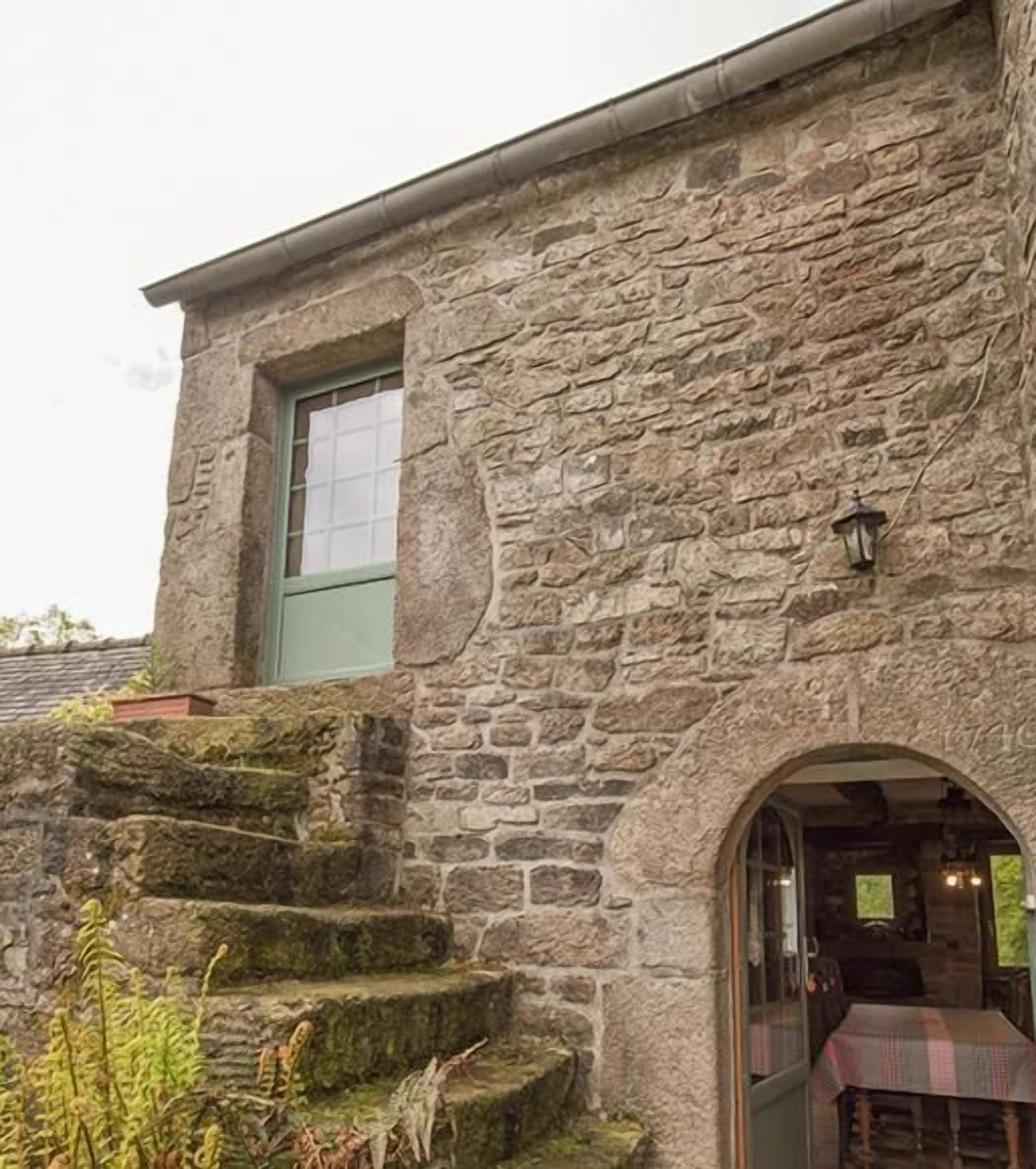 A stone building with a window and a door, a staircase leading up to the entrance, and a table set up outside.