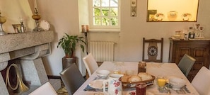 A dining area with a table set for four, a potted plant, and a window with a view of greenery. - ty dreux (Saint-Thegonnec Loc-Eguiner)