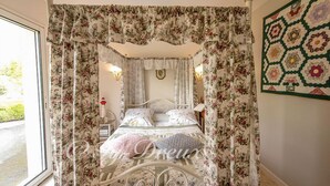 Ein Himmelsbett mit floralen Vorhängen, einem gesteppten Kopfteil und zwei Wandleuchten zum Lesen.