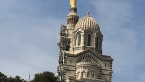 Un grand bâtiment surmonté d’une imposante statue dorée, doté d’un dôme et présentant des détails architecturaux complexes.