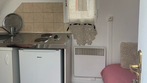 Une cuisine de taille réduite, équipée d’une cuisinière, d’un réfrigérateur et d’une fenêtre agrémentée d’un rideau décoratif.