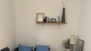 Une chambre à coucher comprenant un lit, des oreillers, une table de chevet, une lampe, une plante en pot et une étagère avec des objets décoratifs.