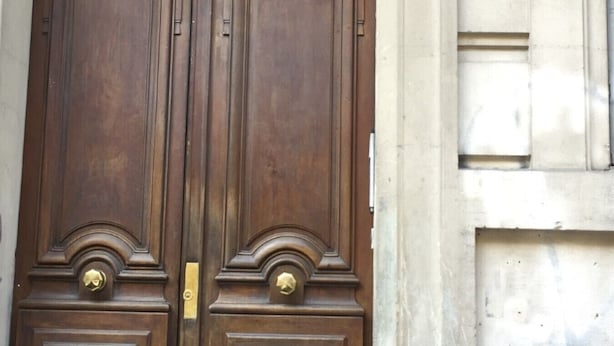Une porte à deux battants en bois, dotée d’une poignée en laiton et d’une grille métallique décorative au-dessus.