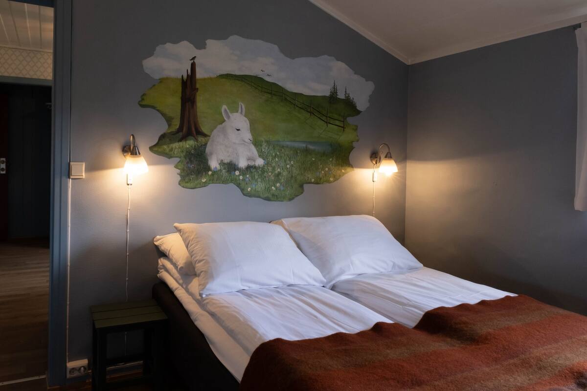 A bedroom with a bed, a wall mural, and two wall-mounted lamps.