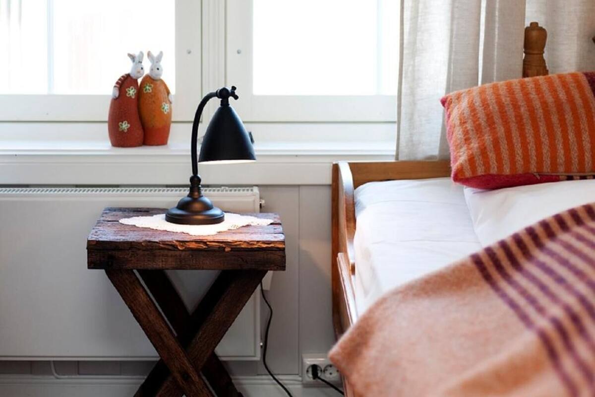 A bedroom with a wooden bed, a bedside table with a lamp, and a window with curtains.