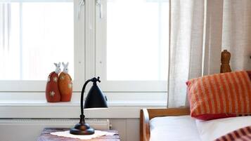 A bedroom with a wooden bed, a bedside table with a lamp, and a window with curtains.
