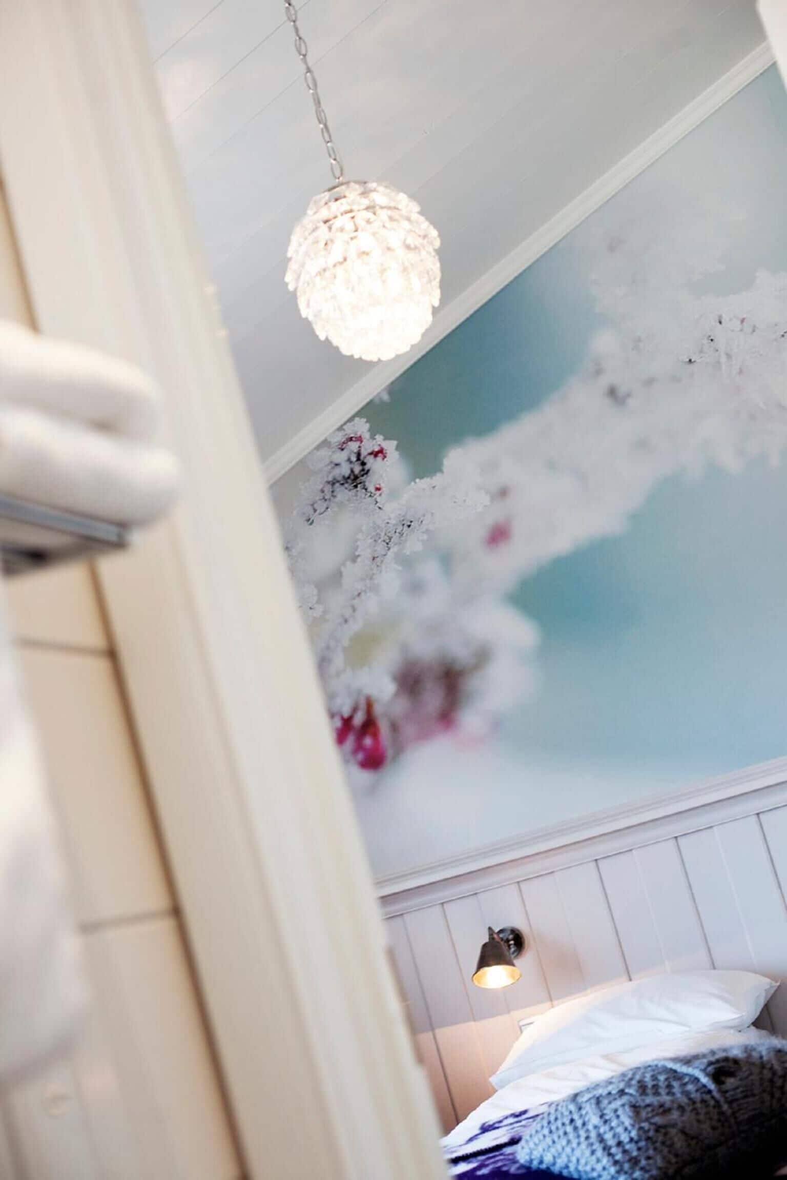 A bedroom with a white bed, a hanging light fixture, and a wall with a floral design.