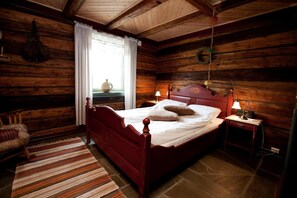 Un dormitorio de cabaña de madera con una cama, una mesita de noche, una lámpara y una silla.