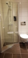 Cabina de ducha con paredes de vidrio, un cabezal de ducha de mano y un grifo montado en la pared.