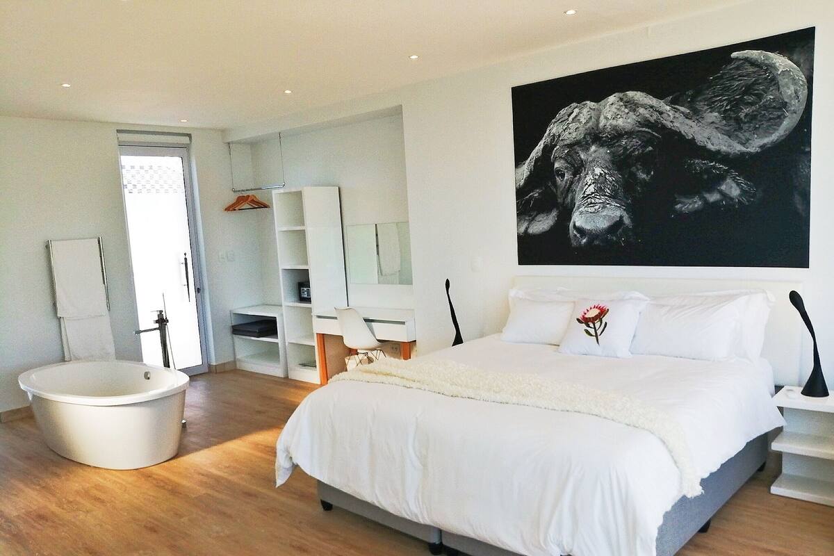 Un dormitorio moderno con una cama grande, una bañera y un cuadro de gran tamaño en la pared.