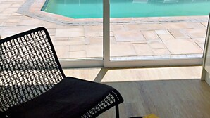 A room with a view of a swimming pool, a black chair, and a small table with a book titled "Awesome South Africa". - Peach on Beach Boutique Guesthouse (Cape Town)