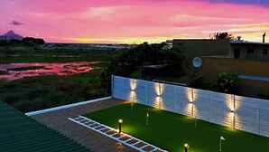 A landscaped area with a pathway, a flag, and a view of a sunset over a landscape with a mountain in the distance. - Peach on Beach Boutique Guesthouse (Cape Town)