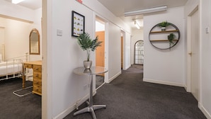 Un couloir comprenant un lit, une petite table avec une plante et une étagère murale ornée de plantes.